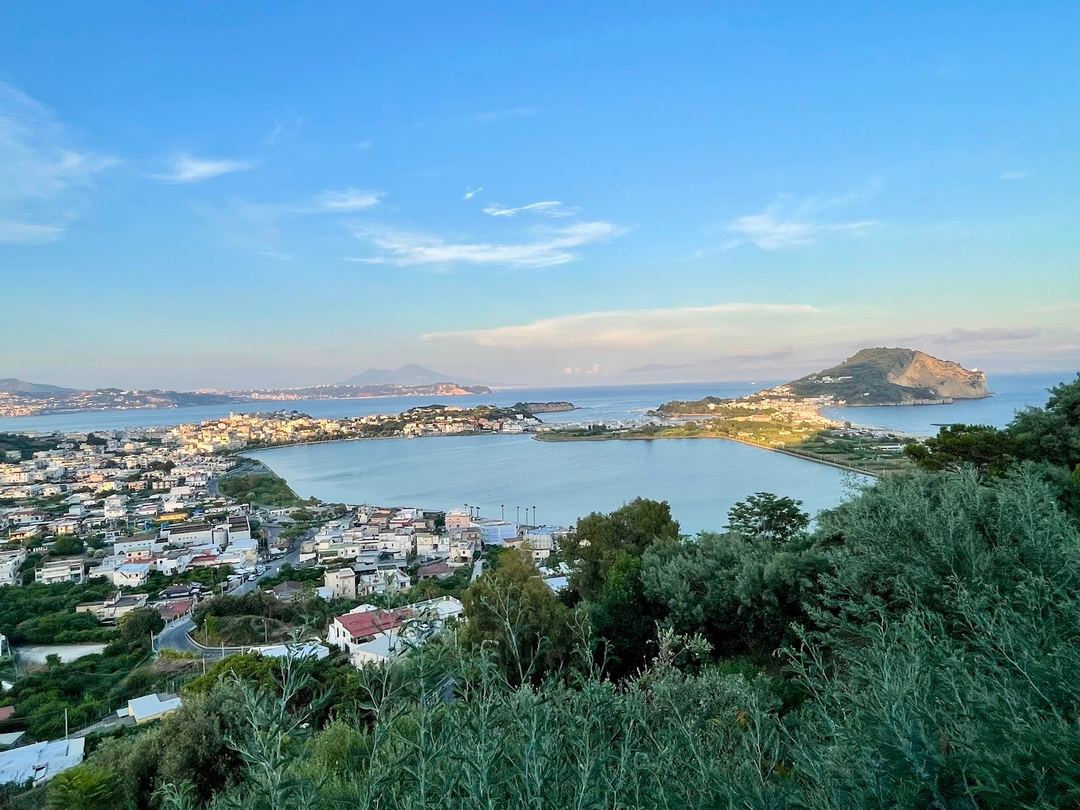 Panoramic view of the Bay of Naples with Vesuvius volcano in the distance, volcanic islands, and coastal settlements nestled along the shoreline.